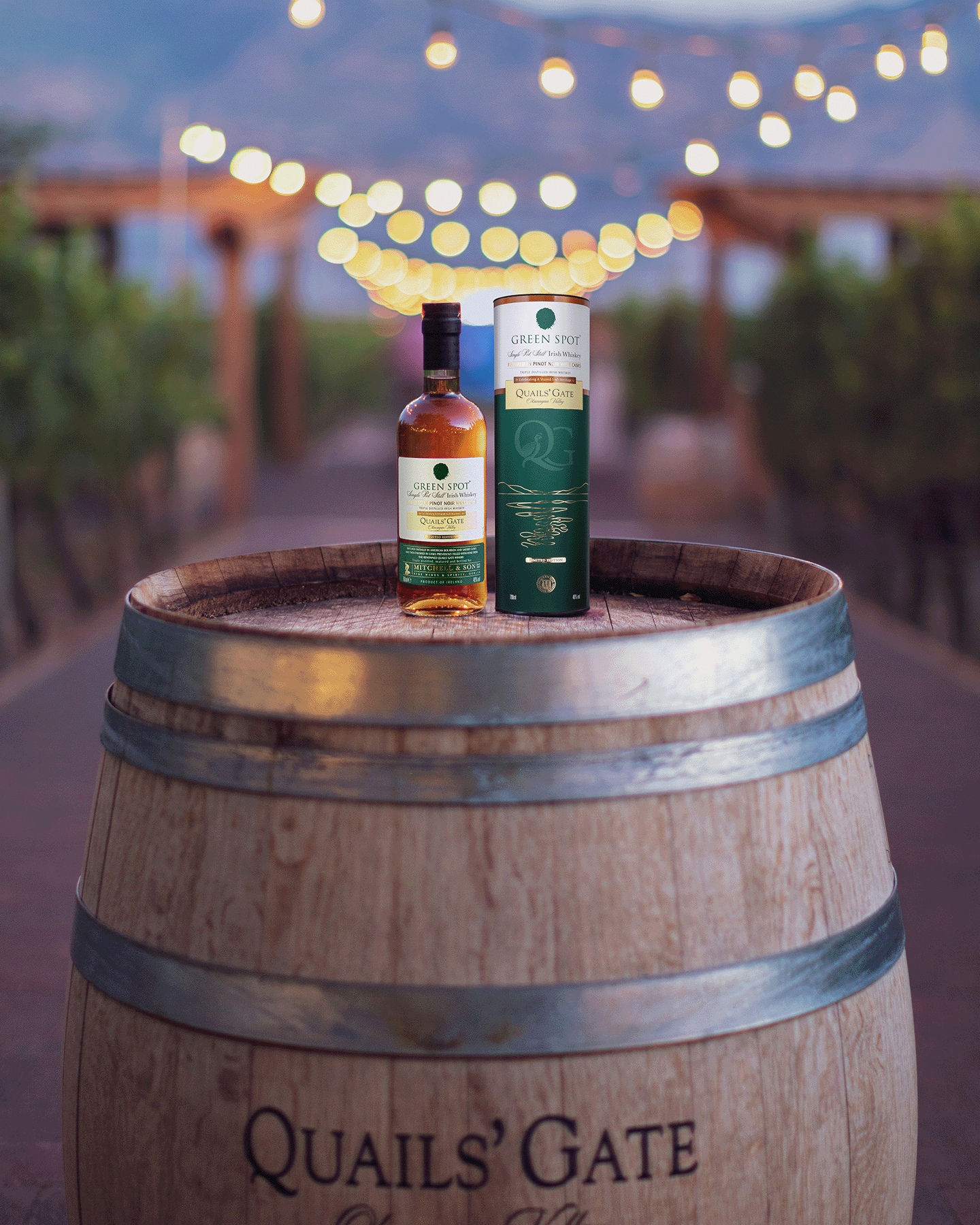 Green Spot Quails Gate Whiskey on top of a barrel with fairy lights and an alleyway in the background
